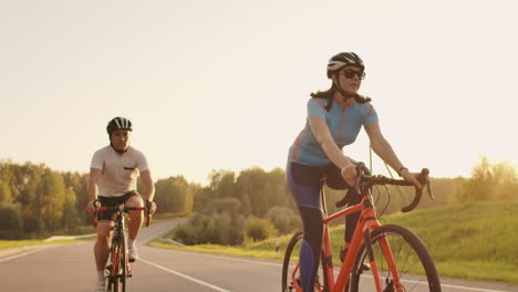 A-man-and-a-woman-on-bicycles-ride-down-the-road-at-sunset-together-in-slow-motion.-The-couple-travels-by-Bicycle.-Sports-Cycling-helmets.